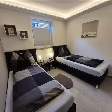 A modern bedroom with two single beds. The decor is simple and in neutral colors.