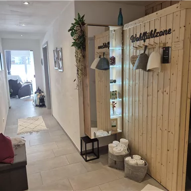 An inviting hallway with bright walls and a wooden area. To the right is a wellness zone with decoration and a relaxation bench.