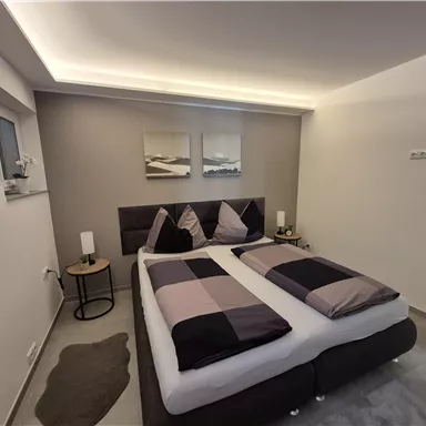 A modern bedroom with a double bed and stylish pillows. The walls are painted in neutral colors, and there is soft lighting.