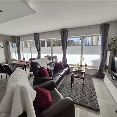 A modern living room with comfortable furniture and large windows. The room is bright and friendly, with decorative elements and a cozy atmosphere.