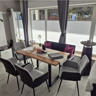 A modern dining room with a wooden table and six chairs. Large windows let in plenty of light and create a bright atmosphere.