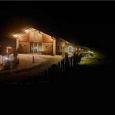 Ein elegantes Gebäude in der Nacht, beleuchtet von warmem Licht. Es liegt in einer verschneiten Umgebung mit einer einladenden Atmosphäre.