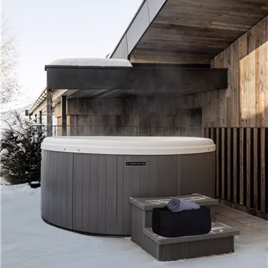 Ein Whirlpool im Freien, umgeben von Schnee. Die Holzverkleidung des Hauses sorgt für eine gemütliche Atmosphäre.