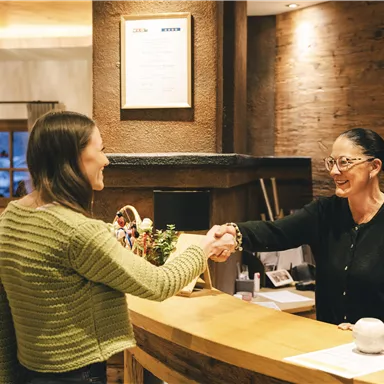 A friendly greeting at the reception. A woman shakes hands with the reception lady, while a young man watches.