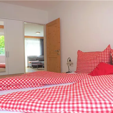 A cozy bedroom with a double bed and red-and-white checked bedding. The room has a wardrobe and plenty of daylight.