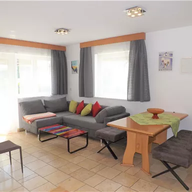 A bright living room with a gray sofa and colorful cushions. A table with chairs complements the cozy space.