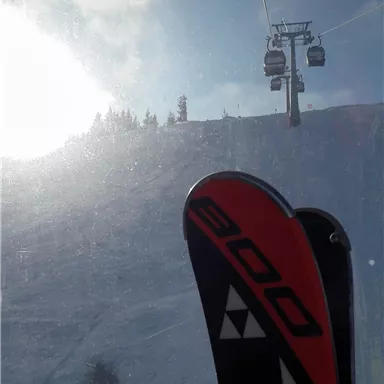 Ski und eine Seilbahn sind im Bild zu sehen. Der Himmel ist teilweise bewölkt und es liegt Schnee auf dem Hang.