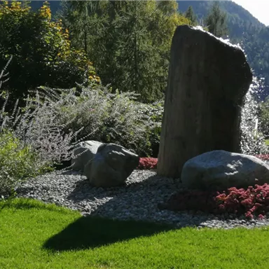 Ein schöner Garten mit einem großen Stein und bunten Blumen. Grüne Rasenflächen und Sträucher umgeben die Steine.