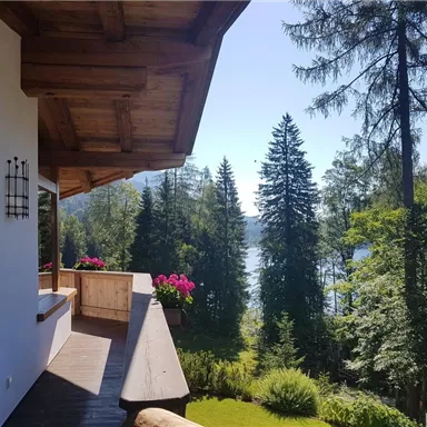 Ein schöner Ausblick von einer Terrasse mit Blumen und grünen Bäumen. Im Hintergrund ist ein klarer See und ein blauer Himmel zu sehen.