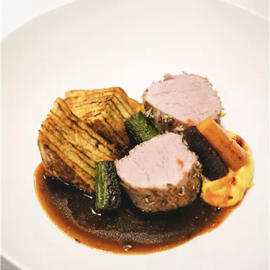 A creatively arranged dish with tender meat, sautéed vegetables, and a dark sauce. Served with potatoes in the form of slices.