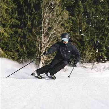 A skier is gliding through the snow in a forest. The surroundings are wintry and the trees are green.