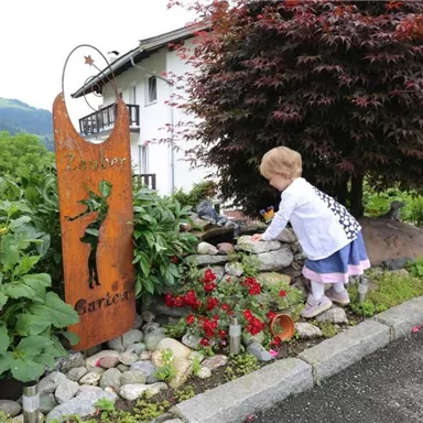 Ein kleines Mädchen spielt in einem Garten mit bunten Blumen und Pflanzen. Im Hintergrund steht ein dekoratives Schild.