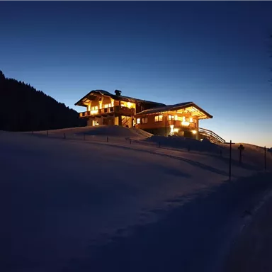 A cozy house in the snow, illuminated by warm light. The sky is in soft twilight colors.