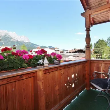 A cozy balcony with blooming plants and a view of the mountains. The wood paneling and the chair invite you to relax.