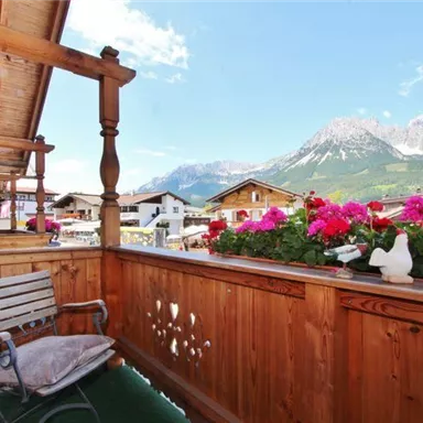 A beautiful balcony with a wooden railing and blooming flowers. In the background, majestic mountains and a clear sky can be seen.