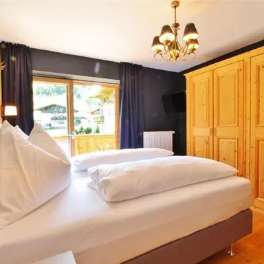 A modern bedroom with two beds and a wooden dresser. The window provides a view of the outside surroundings and lets in plenty of daylight.