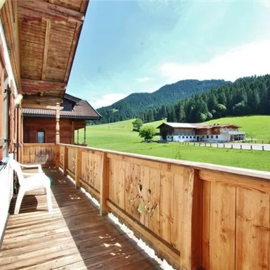 A sunny balcony with a wooden railing and a view of green meadows and mountains. Typical alpine houses can be seen in the background.
