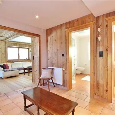 An inviting hallway with wooden walls and terracotta flooring. On the left, there is a cozy living area with a sofa.
