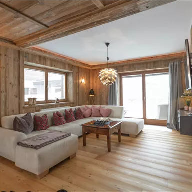 A cozy living room with wood paneling and large windows. An inviting sofa and a modern coffee table create a comfortable atmosphere.