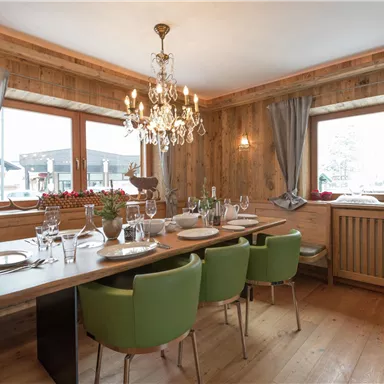 A cozy dining area with wooden walls and an elegant chandelier. The table is set and accommodates several guests.