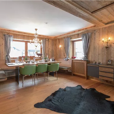 A cozy dining area with wooden paneling and a large table. Green chairs and an elegant lamp create an inviting atmosphere.