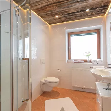 A modern bathroom with a shower cabin and a sink. Bright walls and a wooden ceiling create an inviting atmosphere.