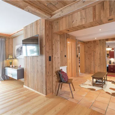 A cozy interior with wooden paneling and an open living area. In the background, a modern kitchen can be seen.