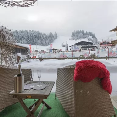 A cozy terrace with two chairs and a glass of ice in the solitude of winter. In the background, one can see snow-covered hills and a picturesque mountain landscape.