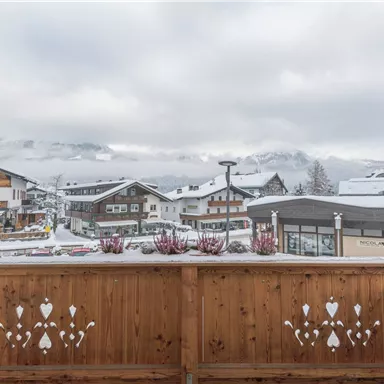 A picturesque view of a snow-covered village with traditional wooden houses. The mountains are enveloped in clouds, creating a cozy atmosphere.