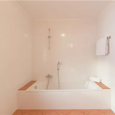 A bright bathroom with a bathtub and warm tiles. The walls are tiled in white, and a towel hangs on the wall.