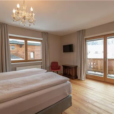 A cozy bedroom with a double bed and large windows. The room is bright and modernly furnished, with access to a balcony.