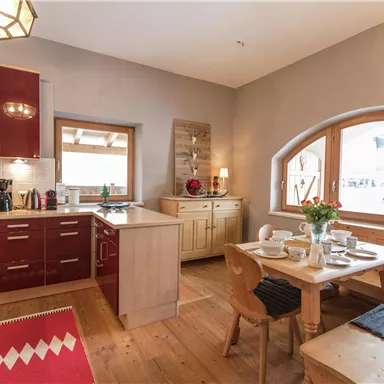A modern kitchen with red cabinets and wooden surfaces. An adjacent dining area with a table and chairs is well set.