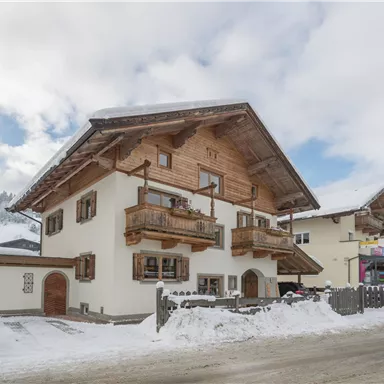 A cozy wooden house in the snow with balconies. The surrounding mountains are slightly cloudy, giving the scene a wintry atmosphere.
