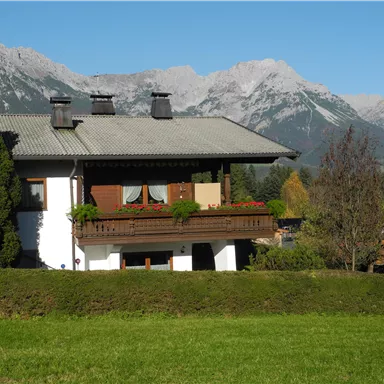 Ein hübsches Haus mit einem Balkon, umgeben von grünen Wiesen. Im Hintergrund sind majestätische Berge zu sehen.