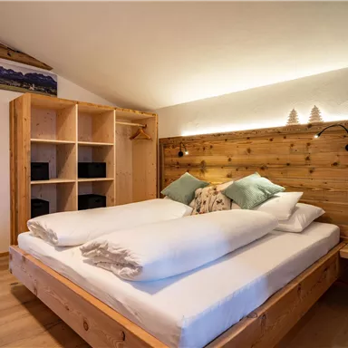 Ein gemütliches Schlafzimmer mit einem großen Holzbett und weichen Kissen. Die Wände sind aus hellem Holz, und es gibt ein Bücherregal im Hintergrund.