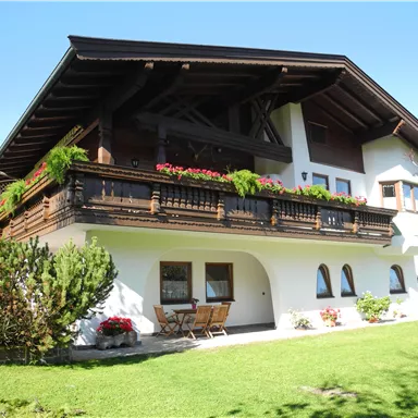 Ein schönes, traditionelles Haus mit einem Balkon voller Blumen. Darum herum gibt es einen gepflegten Garten mit grüner Rasenfläche.