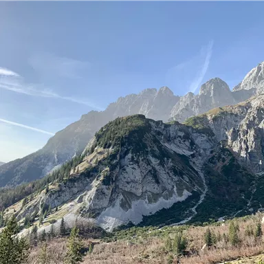 Eine malerische Berglandschaft mit hohen Felsen und klarem Himmel. Das Gebiet ist von Bäumen und grünem Gras umgeben.
