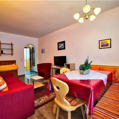 Ein gemütlicher Wohnbereich mit einem Esstisch und bunten Kissen. Die warme Farbauswahl schafft eine einladende Atmosphäre.