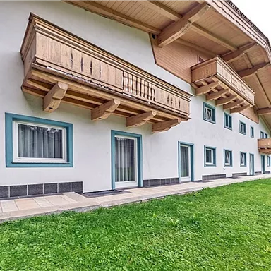 Ein modernes Gebäude mit Holzbalustraden und Balkonen. Der Außenbereich ist von grünem Rasen umgeben.