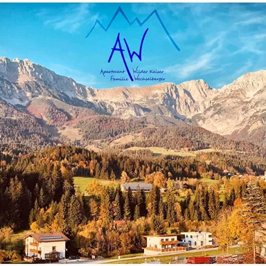 A picturesque mountain landscape with colorful trees in autumn. In the foreground, small houses and a clear sky can be seen.