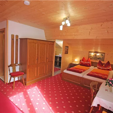 Ein gemütliches Zimmer mit Holzverkleidung und zwei Betten. Der Raum ist freundlich eingerichtet mit einem Tisch, Stühlen und einer Blume auf dem Tisch.