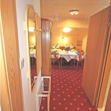 Ein Flur mit Holzdecken und Teppichboden. Im Hintergrund sieht man einen Tisch mit gedeckten Tellern und Dekoration.