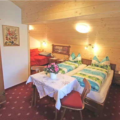 Ein gemütliches Schlafzimmer mit zwei Betten und traditionellen Möbeln. Der Raum ist hell erleuchtet und dekoriert mit einem Tisch und Stühlen.