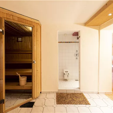 Ein stilvolles Saunainterieur mit einer Holzkabine und einem angrenzenden Duschbereich. Der Raum ist hell und einladend gestaltet.