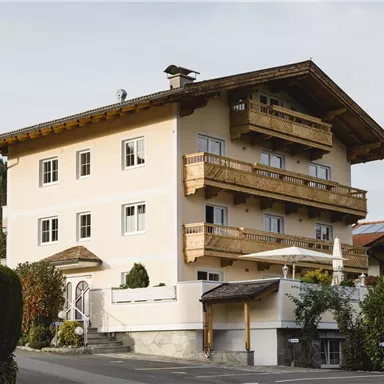 Ein modernes Mehrfamilienhaus mit holzverzierten Balkonen. Es liegt in einer ruhigen Umgebung mit gepflegten Gärten und Bäumen.