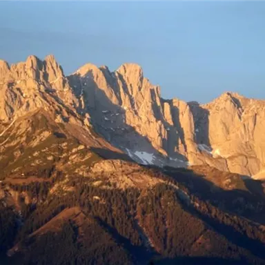 An impressive mountain landscape with high, rugged peaks. The golden light of the evening sun bathes the rocks in warm hues.
