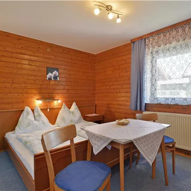 Ein gemütliches Zimmer mit Holzvertäfelung, zwei Betten und einem Tisch. Das Fenster bietet Tageslicht und einen Blick nach draußen.