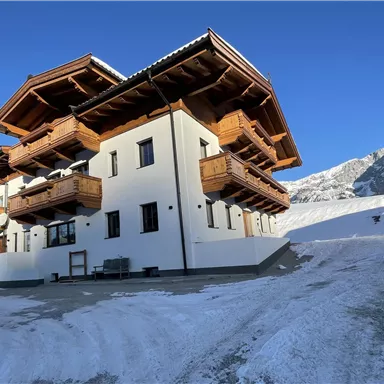 A modern building in alpine style, surrounded by snow and mountains. The balconies are made of wood, giving the house a cozy charm.