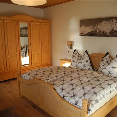 Ein gemütliches Schlafzimmer mit einem großen Bett und traditionellen Holzmöbeln. Der Raum hat eine warme Atmosphäre und eine schöne Berglandschaft an der Wand.