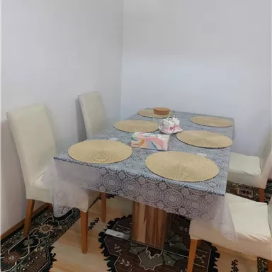 A dining area with a wooden table and white chairs. The table is decorated with a tablecloth and coasters.